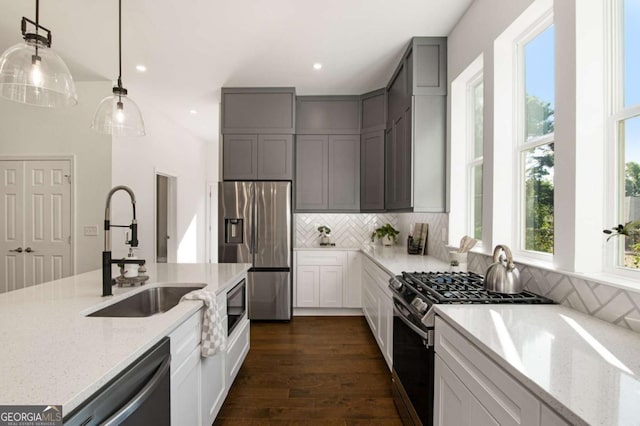 kitchen with stainless steel appliances, light stone countertops, pendant lighting, dark wood-type flooring, and sink