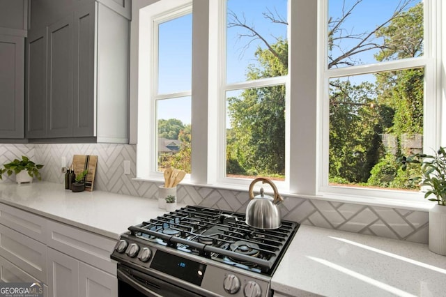 kitchen featuring gas range oven, gray cabinets, backsplash, and light stone counters