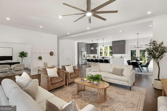 living room with ceiling fan with notable chandelier, beam ceiling, wood-type flooring, and sink