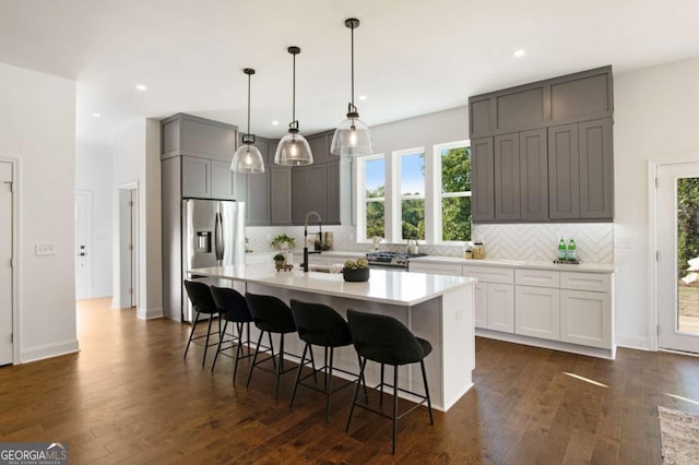 kitchen featuring gray cabinetry, stainless steel appliances, an island with sink, a breakfast bar, and decorative light fixtures