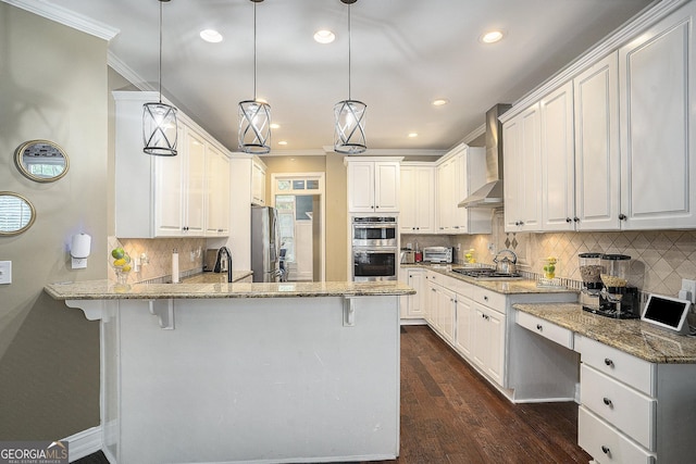 kitchen featuring a breakfast bar area, wall chimney range hood, pendant lighting, and white cabinetry