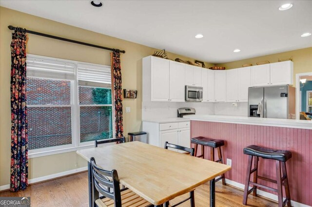 kitchen with white cabinets, stainless steel appliances, light hardwood / wood-style floors, and a kitchen breakfast bar