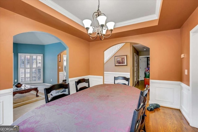 dining area with an inviting chandelier, a raised ceiling, ornamental molding, and light hardwood / wood-style floors