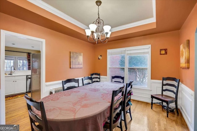 dining room featuring a raised ceiling, light wood-type flooring, a notable chandelier, radiator heating unit, and sink