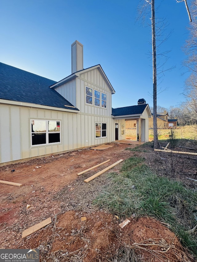 rear view of property with a chimney, board and batten siding, and roof with shingles