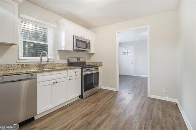 kitchen with white cabinets, stainless steel appliances, light stone counters, and sink