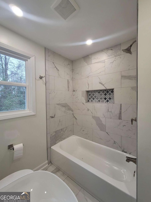 bathroom with toilet and tiled shower / bath