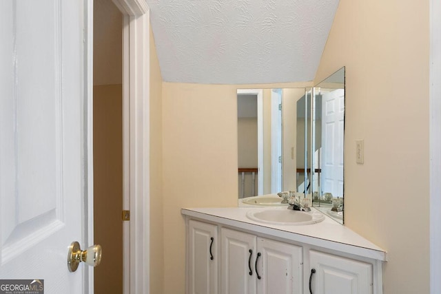 bathroom with a textured ceiling, lofted ceiling, and vanity