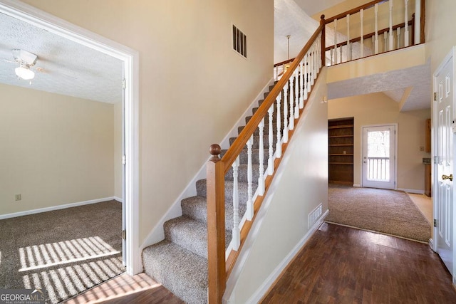 stairs with a towering ceiling, a textured ceiling, ceiling fan, and hardwood / wood-style flooring