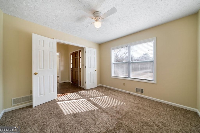 unfurnished bedroom with ceiling fan, a textured ceiling, and dark carpet