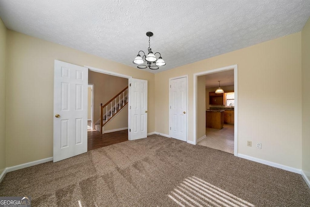 carpeted empty room featuring a textured ceiling and a chandelier