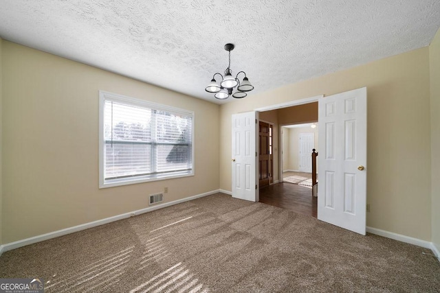 unfurnished room with a textured ceiling, a chandelier, and dark carpet