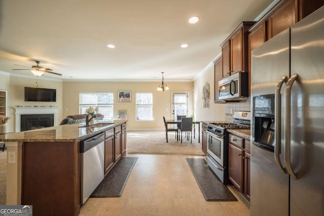 kitchen featuring pendant lighting, a kitchen island with sink, light stone countertops, appliances with stainless steel finishes, and ceiling fan with notable chandelier