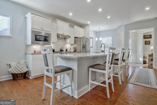 kitchen featuring a center island with sink, light hardwood / wood-style floors, stainless steel appliances, white cabinetry, and tasteful backsplash