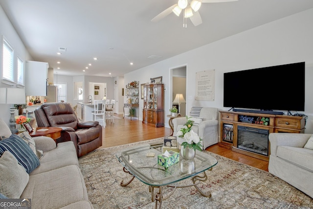 living room featuring light hardwood / wood-style floors, ceiling fan, and a fireplace