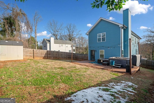 rear view of property with a lawn, a patio area, a hot tub, and a storage shed