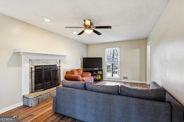 living room with a stone fireplace, ceiling fan, and dark hardwood / wood-style floors