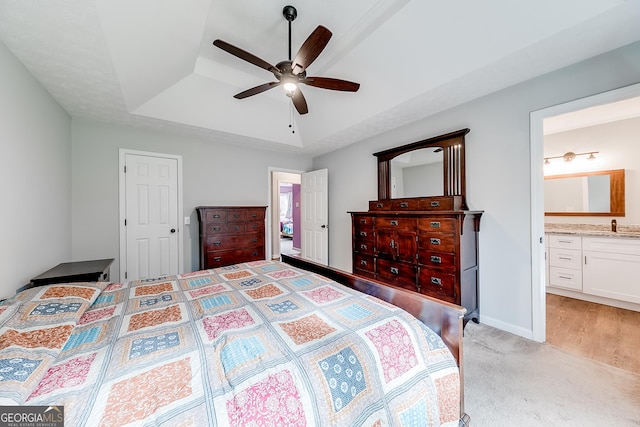 bedroom with connected bathroom, sink, light carpet, a tray ceiling, and ceiling fan