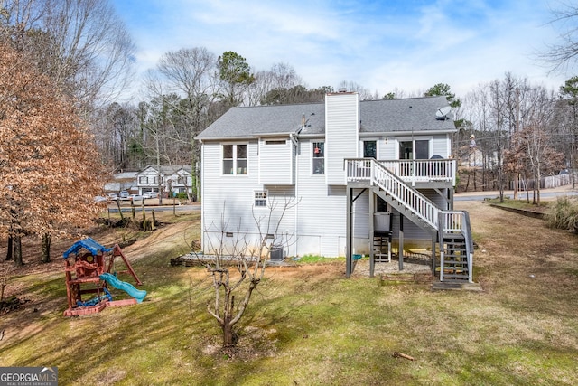 back of house with central AC unit, a playground, a deck, and a lawn