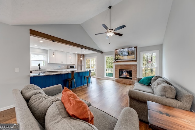 living room with sink, ceiling fan, high vaulted ceiling, wood-type flooring, and a fireplace