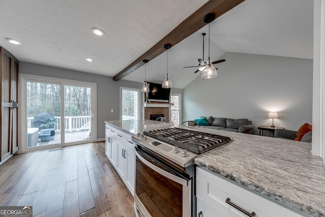 kitchen with stainless steel gas stove, light stone counters, white cabinets, decorative light fixtures, and light wood-type flooring