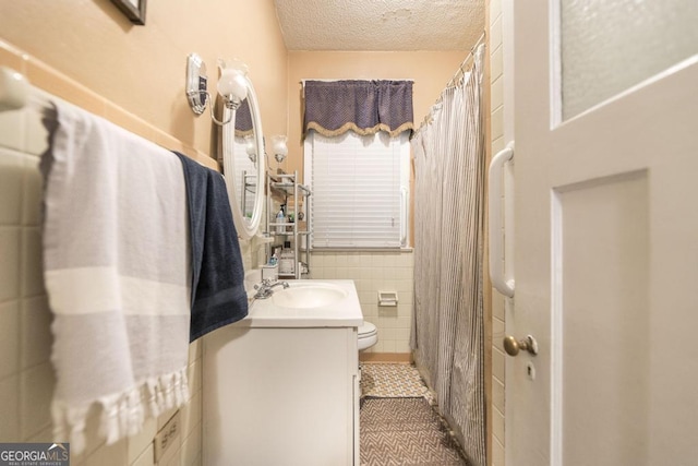 bathroom with a textured ceiling, tile patterned flooring, tile walls, toilet, and vanity