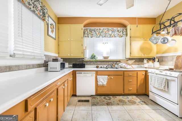 kitchen with white appliances, hanging light fixtures, light tile patterned floors, backsplash, and sink