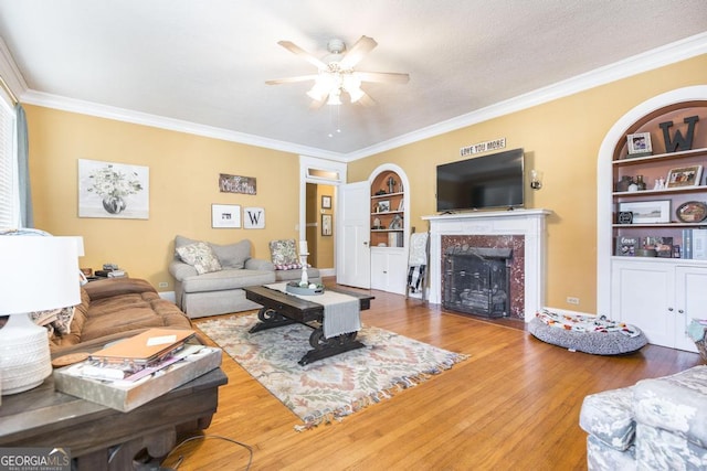 living room with hardwood / wood-style flooring, ornamental molding, built in shelves, a fireplace, and ceiling fan