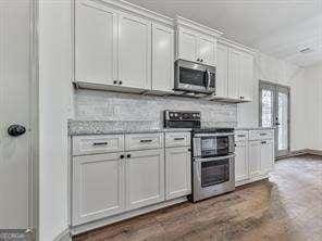 kitchen featuring white cabinets, light stone counters, french doors, tasteful backsplash, and appliances with stainless steel finishes