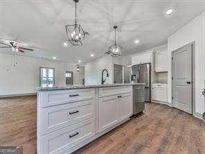 kitchen featuring a center island with sink, dark wood-type flooring, white cabinets, decorative light fixtures, and sink