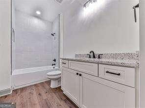 full bathroom with toilet, tiled shower / bath, hardwood / wood-style floors, and vanity