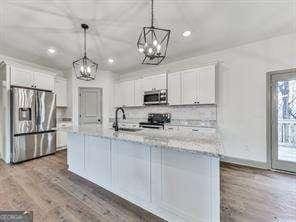 kitchen featuring stainless steel appliances, white cabinetry, hanging light fixtures, and an island with sink