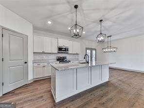 kitchen featuring stainless steel appliances, white cabinets, a kitchen island with sink, and hanging light fixtures