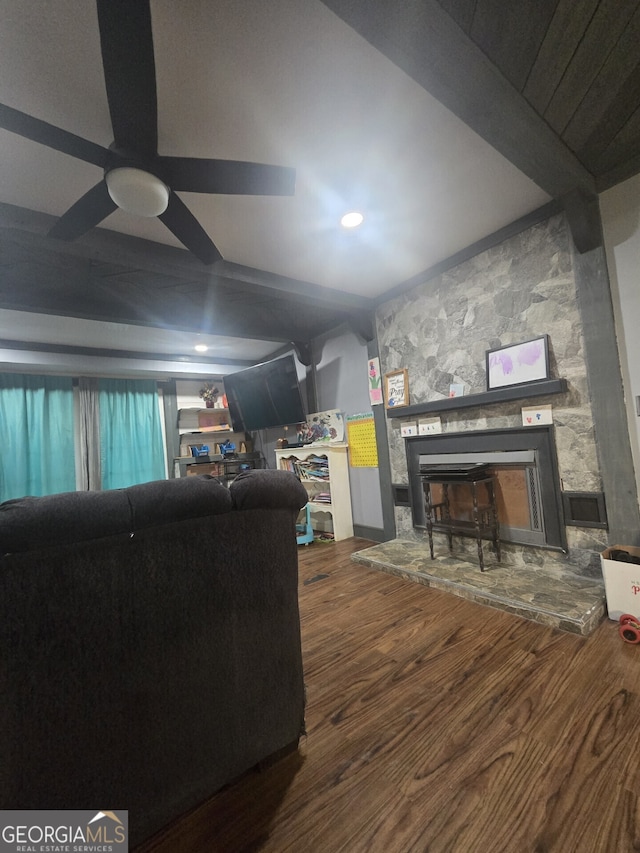 living room with hardwood / wood-style floors, built in features, ceiling fan, beamed ceiling, and a stone fireplace