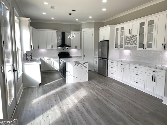 kitchen with decorative light fixtures, white cabinetry, light stone counters, stainless steel refrigerator, and wall chimney range hood