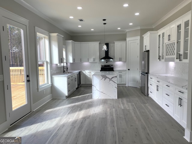 kitchen featuring decorative light fixtures, white cabinets, and wall chimney range hood