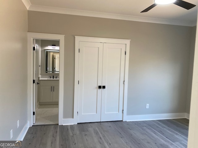 unfurnished bedroom featuring a closet, ensuite bath, light hardwood / wood-style floors, crown molding, and ceiling fan