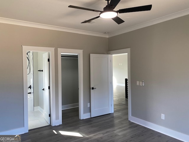 unfurnished bedroom featuring ensuite bath, ceiling fan, dark wood-type flooring, a spacious closet, and ornamental molding