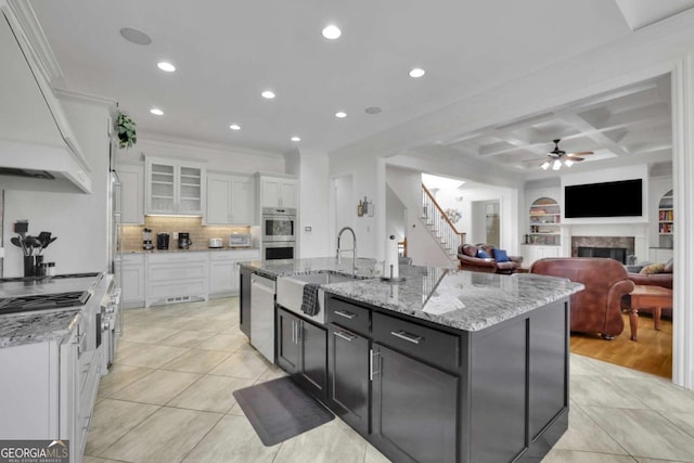 kitchen with ceiling fan, a kitchen island with sink, stainless steel appliances, custom range hood, and white cabinets