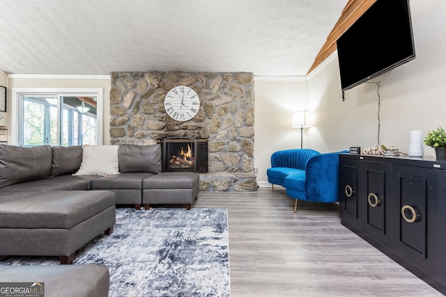 living room featuring light wood-type flooring, a fireplace, crown molding, and a textured ceiling