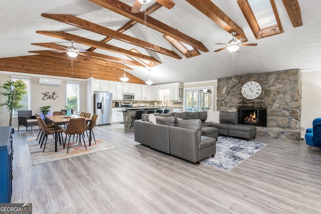 living room with a stone fireplace, ceiling fan, a wall mounted air conditioner, high vaulted ceiling, and light hardwood / wood-style flooring