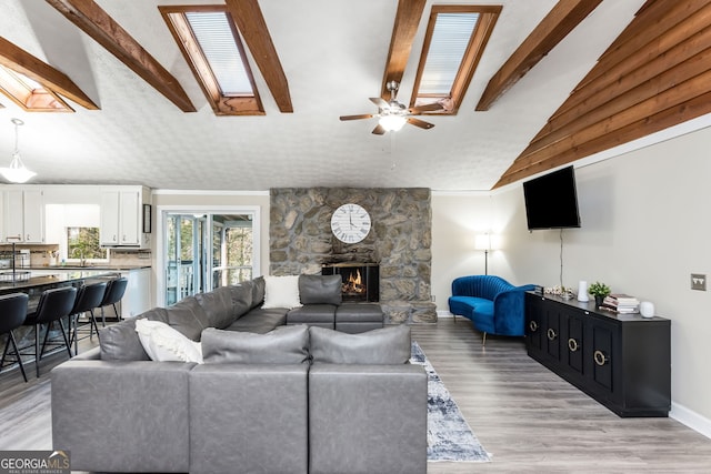 living room with light hardwood / wood-style floors, ceiling fan, vaulted ceiling with skylight, a fireplace, and sink