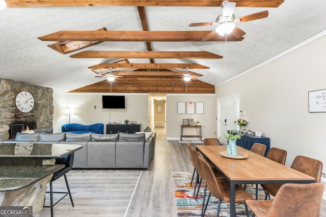 dining area with hardwood / wood-style flooring, ceiling fan, a fireplace, high vaulted ceiling, and beam ceiling