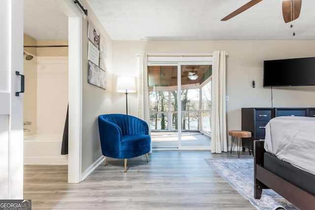 bedroom featuring ceiling fan, a barn door, access to outside, light wood-type flooring, and connected bathroom