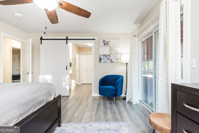 bedroom with ceiling fan, a barn door, light hardwood / wood-style floors, a textured ceiling, and a closet