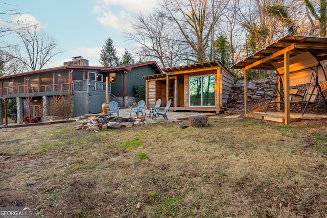 rear view of house featuring a lawn, an outdoor fire pit, and a sunroom