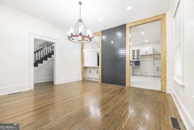 unfurnished dining area featuring an inviting chandelier, crown molding, and dark hardwood / wood-style floors