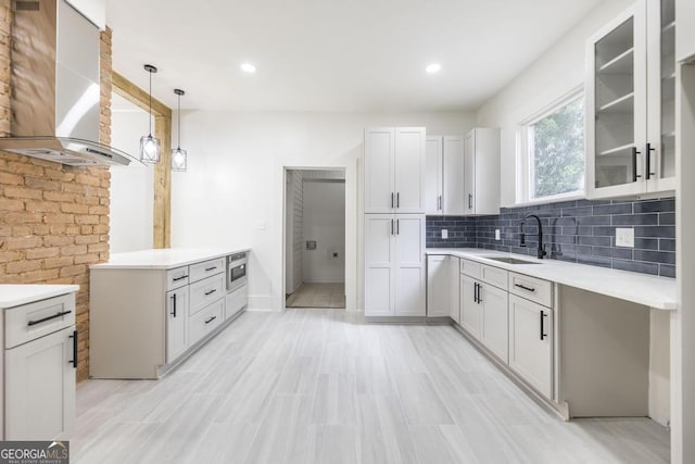 kitchen featuring range hood, decorative light fixtures, white cabinetry, and sink