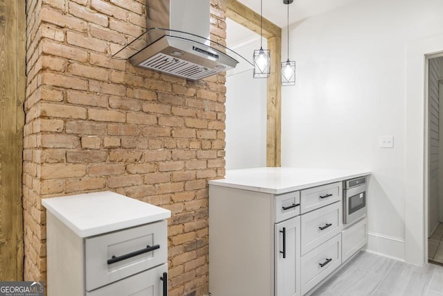 interior space with brick wall, island range hood, stainless steel microwave, and hanging light fixtures