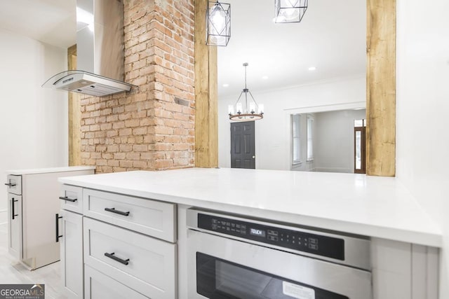 kitchen with an inviting chandelier, crown molding, white cabinets, decorative light fixtures, and range hood